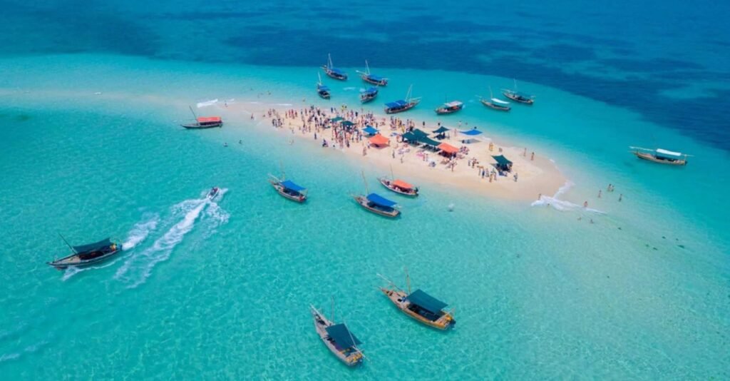 Traditional dhow boat during the Safari Blue Tour in Zanzibar with guests snorkeling in crystal-clear waters and relaxing on a tropical sandbank.